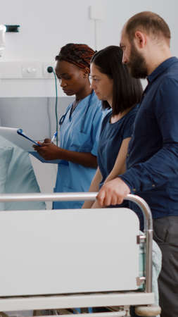 Physician pediatric doctor monitoring disease symptoms while african american nurse checking IV drip...