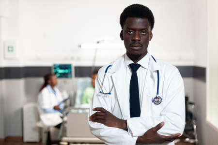 Portrait of african american doctor looking at camera in hospital ward. Black man with coat and stethoscope with medical recovery occupation. Professional healthcare clinic surgeon, medicの写真素材