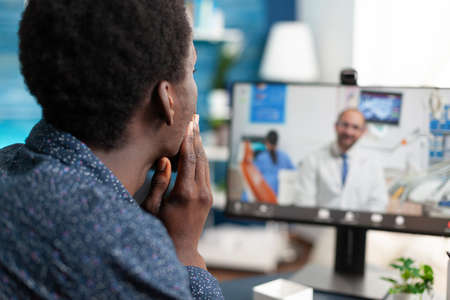 Online healthcare checkup of african american guy talking with family doctor using internet app sitting at home. Black man doing telemedicine consultation for patient prescription treatmentの写真素材