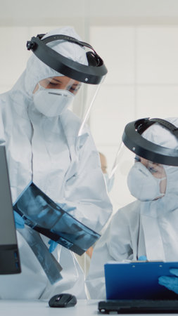 Professional dentist and assistant examining x ray of teeth while sitting in dental cabinet, during...