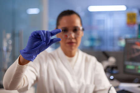 Biotechnology doctor holding sample of blood investigating pattern for innovation treatment in...