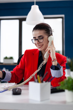 Businesswoman taking notes on clipboard sitting at desk in corporate office, while taking with adviser about financial expertise. Busy manager having a conversation about deadline.の写真素材