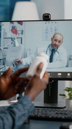 Black man at home seeking medical help from doctor via online intenet telehealth consultation with family doctor. Health care checkup via video virtual conference, patient looking for medicine adviceの写真素材