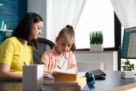Child and parent doing homework together at home writing exercises for elementary lesson. Caucasian...