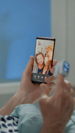 Sick elder patient talking on videocall with family in hospital ward at intensive care unit. Old man with nasal oxygen tube using smartphone to call relatives while on treatmentの写真素材