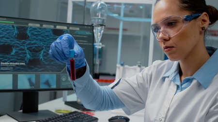 Doctor in science laboratory analyzing tray of vacutainers on desk. Chemistry scientist looking at...