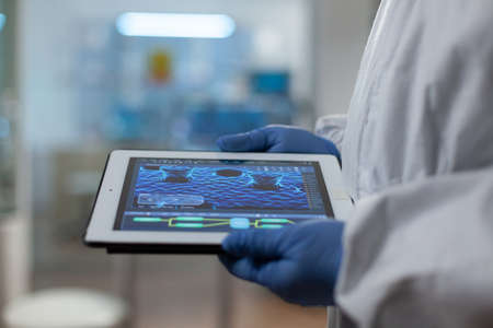 Scientist doctor wearing medical gloves and ppe suit holding tablet in hands analyzing virus...