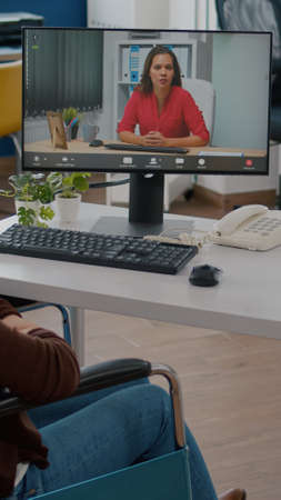 Invalid disabled immobilized entrepreneur talking with remote coworker during video conference,...