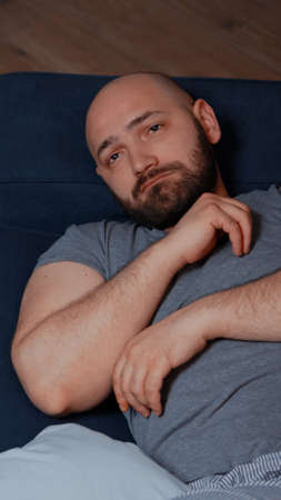 Worried desperate frustrated sad alone man suffering from big depression loneliness familly lost, crying lying in sofa staring into space feeling disappointment frustration pain vulnerable traumatisedの写真素材