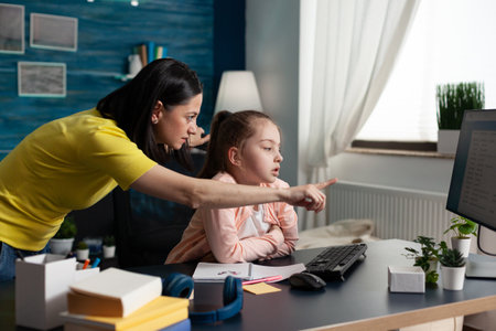 Mother teaching little pupil about school lesson at home for educational success indoors. Parent doing elementary homework assisting child on studying online using computer internetの写真素材