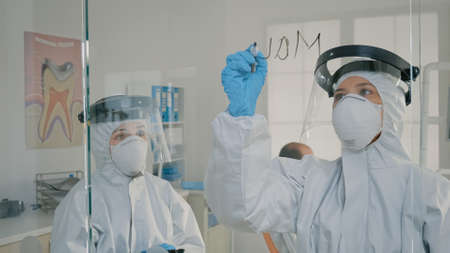 Dental specialists analyzing tablet screen and writing on glass for information of teethcare...