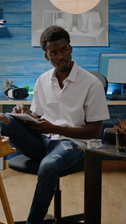 Man of african american ethnicity designing sketch for vase drawing on white canvas and easel in...