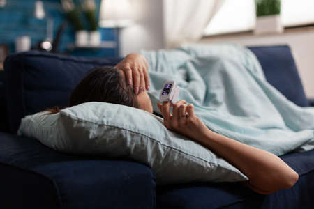 Sick woman on sofa using medical technology for pandemic coronavirus. Caucasian adult with pulse...