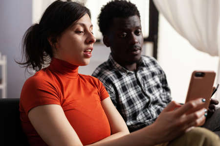 Close up of modern interracial couple using smartphones at home. Multi ethnic partners holding digital devices with technology. Mixed race people having gadgets with online internet.の写真素材