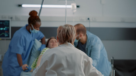 Doctor and african american nurse helping pregnant woman with painful childbirth in hospital ward. Young caucasian person giving birth while getting medical support and assistanceの写真素材