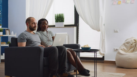 Interracial couple using video call communication at home talking to friends on laptop. African...