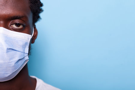 Close up of eye of african american adult wearing face mask while looking at camera in studio. Black face with protection against coronavirus for healthcare, standing over isolated backgroundの写真素材