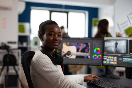 African american video editor artist looking at camera smiling editing creative video project in post production software working in startup studio office. Videographer editing audio film montageの写真素材
