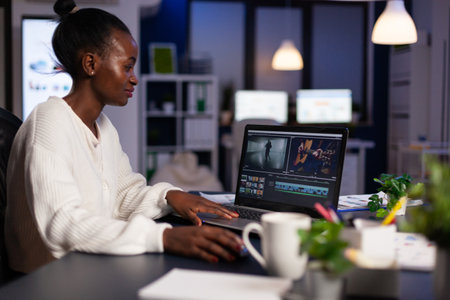 African american video editor working late at night at digital movie project editing audio film montage in in creativity start-up business office. Videographer using post production softwareの写真素材