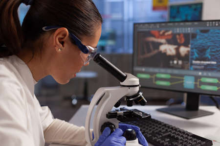 Biochemist working on microscope for cell illustration on computer screen in chemical laboratory....