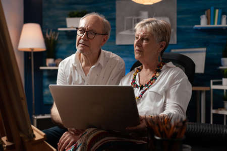 Professional artists using laptop for artistic inspiration at studio. Senior man and woman looking...