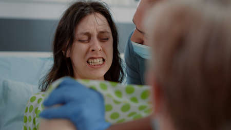Close up of pregnant woman pushing and screaming in hospital ward at clinic. Young person giving birth while being in pain. Caucasian husband supporting wife with contractions and childbirthの写真素材