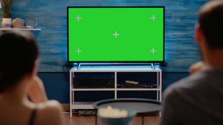 Young adults looking at modern technology green screen on television at home. Caucasian people with copy space and virtual chroma key for isolated template or mockup backgroundの写真素材