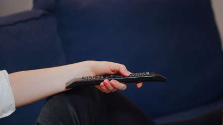 Close up of hand holding remote for television while laying on couch. Caucasian person switching...
