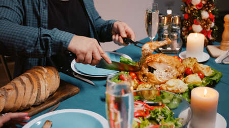 Close up of man cutting meal at christmas dinner celebration. Adult preparing chicken for woman, enjoying festive food and drinking champagne. Holiday festivity with food and alcoholの写真素材