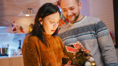 Woman receiving present from man on christmas day. Man giving gift box with ribbon and bow tie to partner, feeling cheerful about holiday season. Couple celebrating winter festivityの写真素材