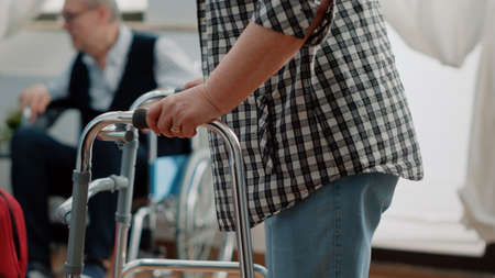 Close up of senior patient with disability using walk frame for mobility and walking in nursing home. Nurse giving assistance and support to old disabled person for physical recoveryの写真素材