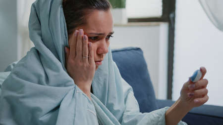 Close up of person with flu looking at thermometer, checking temperature and feeling cold. Woman...