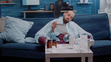 Tired ill person reading medication leaflet to cure cold and flu with prescription treatment. Man...