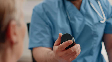 Close up of nurse hand holding bottle of pills and capsules for elder patient sitting in nursing...
