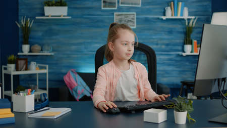 Elementary school child using computer and keyboard at desk for homework and learning. Little girl looking at monitor for online remote class lessons on internet connection at home.の写真素材