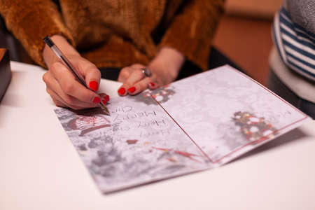 Closeup of woman hands writing xmas greeting card for family during christmas holiday standing in xmas decorated kitchen. Happy family enjoying spending winter season togetherの写真素材