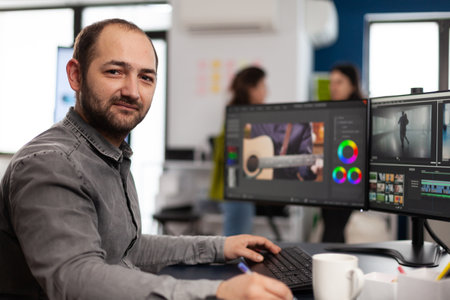 Creative designer artist man looking at camera smiling working in creativity multimedia startup office using editing post production software on professional pc. Processing video film montage.の写真素材