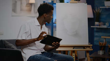 Young african american artist using digital tablet for art drawing project at studio. Black man with creativity skill holding device for modern masterpiece and professional fine artの写真素材