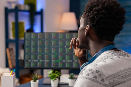 African american trader worker checking stock market chart on computer developing investment strategy. Young man broker trading crypto currency working remote from home. Investment data on screenの写真素材