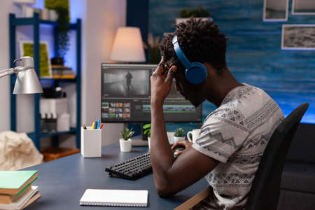 African american videomaker retouching film footage using editing post production sofware working at visual effects for multimedia project. Young videographer sitting at desk looking at movieの写真素材