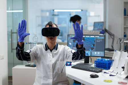 Biologist researcher wearing virtual reality headset examining biochemistry experiment working in microbiology hospital laboratory using biotechnology. Specialist scientist analyzing virus developmentの写真素材