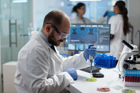 Scientist biologist man putting chemical fluid in petri dish using medical micropippete analyzing bacteria sample liquid. Microbiologist researcher doing biological experiment in medicine hospital labの写真素材