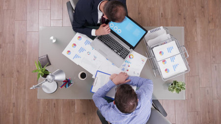 Top view of businessman explaining company charts to partner using laptop while discussing financial statistics during business partnership. Entrepreneur working at management investment in officeの写真素材