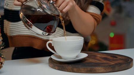 Close up of pouring beverage from tea kettle at festive home. Happy woman preparing for christmas...