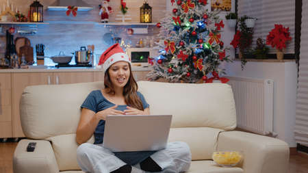Woman using video call communication on laptop for remote christmas celebration with family. Festive...