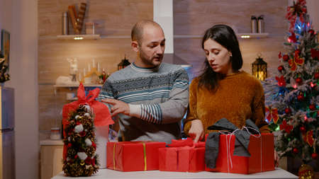 Man bringing presents to sort for family on christmas eve. Couple preparing with gift boxes, ribbon...