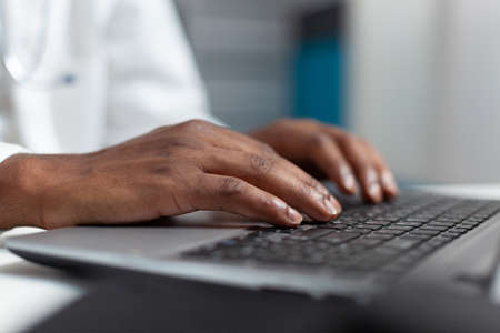 Closeup of african american doctor hand typing healthcare treatment on laptop computer keyboard after analyzing sickness expertise. Practitioner working in hospital office. Health care serviceの写真素材