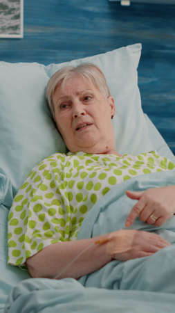 Doctor doing healthcare consultation with retired patient in bed at nursing home. Aged woman with illness talking to specialist about healing treatment and recovery with medicationの写真素材