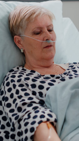Woman with sickness waiting for medical treatment in bed. Healthcare assistant visiting retired patient in hospital ward, with oximeter to measure oxygen saturation for checkup diagnosisの写真素材