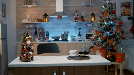 Empty room decorated with ornaments for christmas time with nobody at counter. Kitchen with festive lights, tree and decorations for holiday celebration dinner party with family at homeの写真素材
